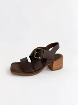 Sandalias de cuero negro con textura croco, punta cuadrada y taco bloque de altura media. Cuenta con tiras cruzadas en el empeine y una hebilla metálica grande decorativa.