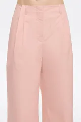 Pantalón tobillero de algodón color beige, de corte recto con cierre frontal de corchete oculto y cremallera, pinzas en la parte delantera y presillas de tela. Presenta bolsillos diagonales delanteros y bolsillos traseros con vivo.