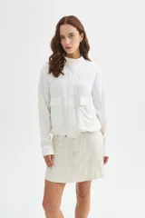 Chaqueta bomber blanca de algodón con cuello mao, bordado sutil, bolsillos frontales con solapa, cierre de botones y cordón ajustable en el ruedo.