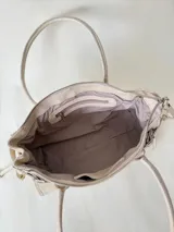 Cartera de cuero de tamaño medio con estructura rígida. Presenta una tira decorativa con tachas y hebillas metálicas en los extremos, además de lazos laterales. Cuenta con doble asa para llevar al hombro y cierre superior.