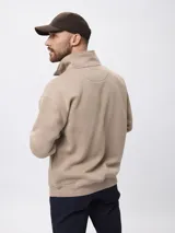 Buzo de felpa color beige, con cuello alto y cierre frontal parcial, de manga larga y diseño holgado.