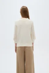 Sweater acrílico en tono natural, de corte holgado, con cuello a la base decorado con sutiles volados, mangas 3/4 y diseño tejido con motivos geométricos calados en el frente.