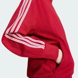 Campera deportiva Adidas color rojo, modelo suelto con cuello alto, cierre frontal completo y bolsillos laterales. Presenta las clásicas tres tiras blancas en las mangas y el logo del trébol bordado en el pecho.