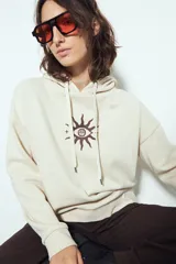 Canguro negro de calce relajado con capucha y cordones ajustables. Presenta un estampado gráfico frontal de un ojo con rayos de sol y la frase "STAY WEIRD".