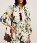 Vestido chemise midi confeccionado en viscosa sostenible, con cuello, abotonadura frontal, recorte en la cintura y bajo fruncido. Presenta un estampado floral con follajes.