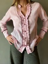 Blusa manga larga color rosa pálido con textura arrugada, cuello mao y volados en el frente con pespunte en color oscuro.