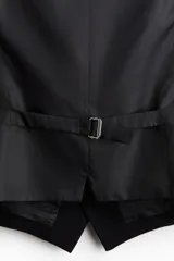 Chaleco de traje formal con cierre frontal de cinco botones y dos bolsillos delanteros ribeteados. Presenta un corte ajustado, forro interior y espalda con tejido brillante y trabilla ajustable.