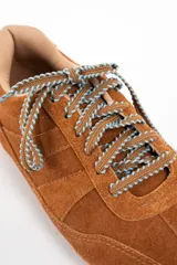 Zapatilla de perfil bajo confeccionada en gamuza color camel, con cordones jaspeados en tonos tierra y suela de goma dentada.