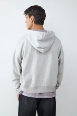 Buzo de algodón gris melange con capucha ajustable mediante cordones, cierre frontal de cremallera y puños y ruedo acanalados.