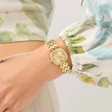 Reloj analógico Guess modelo Hazel con caja cuadrada de 25mm y malla tipo brazalete, todo en tono dorado. La esfera presenta acabado sunray con cristales incrustados en el borde de la caja y en el interior de la esfera.