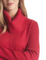 Buzo de punto color beige con cuello volcado amplio, mangas largas acanaladas y torso liso. Presenta una costura central vertical, ruedo con tajos laterales y largo asimétrico, siendo más largo en la parte posterior.