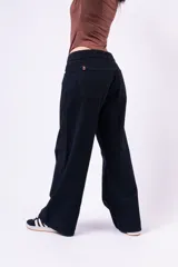 Pantalón wide leg de tiro bajo en color negro, confeccionado en denim, con cierre frontal de botón y bolsillos laterales.