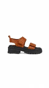 Sandalias de cuero marrón con tiras anchas, detalles en mostaza y suela plana acolchada con cierre de velcro.