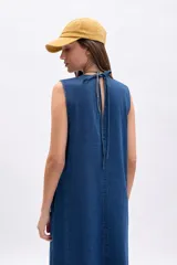 Vestido largo sin mangas de denim azul, con corte recto y holgado, costura central vertical y bolsillos laterales.