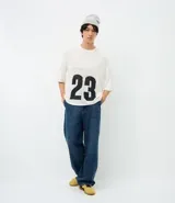 Remera de corte oversized confeccionada en tejido jacquard de color blanco con textura calada. Presenta mangas cortas, cuello redondo y un diseño gráfico deportivo con el número 23 en color negro en la parte frontal.