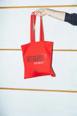 Tote bag de tela color rojo con estampado frontal con la frase 'Is there some reason my coffee isn't here?' y el logo de The Devil Wears Prada.