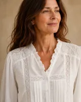 Camisa blanca de manga larga con detalles de encaje, pliegues frontales y cuello con volados.