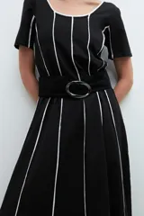 Vestido midi negro con rayas verticales blancas, escote redondo y cinturón negro con hebilla circular.