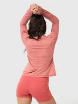 Polera deportiva de manga larga en color rosa melange, con cuello alto y cierre frontal parcial. Presenta un diseño ajustado con costuras visibles y aberturas para los pulgares en los puños.