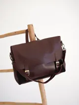 Maletín tipo postman de cuero y gamuza color marrón, con solapa frontal, hebillas metálicas decorativas y correa ajustable para el hombro.