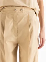 Pantalón slouchy de poplín color beige, de calce regular y largo al tobillo, con tablas en el delantero y ruedo que aportan volumen, bolsillos laterales y cierre con botones tipo honguito.