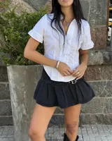 Minifalda tableada de jean color negro, con diseño de tiro bajo y detalle de cinturón integrado con hebilla metálica plateada.