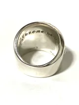 Anillo plateado con diseño de cruz gótica ornamentada con volutas. Fabricado en aleación con baño plateado, acabado envejecido y textura marcada.