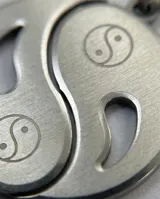 Dije de acero inoxidable con diseño de Yin-Yang, compuesto por dos piezas complementarias que forman un círculo completo, cada una con un símbolo de Yin-Yang grabado.