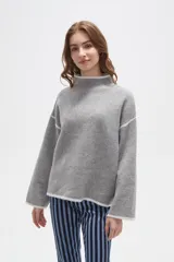 Polera de tejido de punto color negro con detalles de vivos en color beige en el cuello, puños, ruedo y costuras de las mangas. Presenta un diseño holgado con cuello alto y mangas largas.