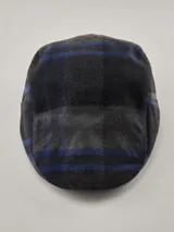 Boina tipo flat cap con diseño de cuadros en tonos gris oscuro y negro, con detalles de líneas en azul. Incluye una etiqueta decorativa lateral de la marca Benson & Thomas.