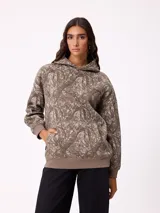 Canguro con capucha de corte holgado, estampado con diseño de ramas en tonos marrones y beige. Presenta bolsillo frontal tipo canguro, puños y ruedo en tejido rib elástico, y logo de la marca bordado en el pecho.