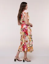 Vestido midi de calce fluido y corte camisero, con estampado floral en tonos rosa, rojo, amarillo y verde. Cuenta con cuello camisero, escote en V, abotonadura frontal oculta, mangas cortas tipo cap sleeve, lazo ajustable en la cintura del mismo género y falda evasé con recorte fruncido.