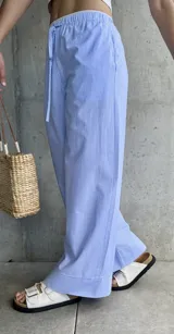 Pantalón pijamero celeste a rayas verticales blancas, de corte ancho y cintura con cordón ajustable.