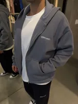Campera con capucha y cierre frontal, de corte boxy y diseño minimalista. Presenta un pequeño logo bordado en el pecho y bolsillos tipo canguro.