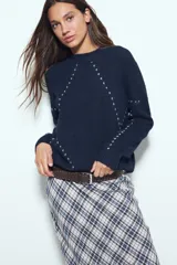 Sweater de tejido suave color marrón con diseño de líneas bordadas en color rojo. Presenta cuello redondo, manga larga y calce relajado.