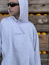 Canguro gris melange con capucha y cordones ajustables en color lila. Presenta el logo bordado en el pecho en color lila y bolsillo frontal tipo canguro.
