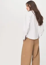 Camisa de popelín de algodón con diseño entallado, cuello camisero, cierre frontal con botones y mangas largas con puños abotonados.