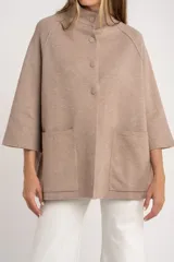 Cárdigan color beige de tejido de punto, con cuello mao, manga 3/4 y cierre frontal con botones. Tiene bolsillos de parche delanteros y corte holgado.