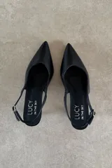 Zapato destalonado Suki de cuero vacuno negro, con taco fino bajo, punta fina y tira ajustable con hebilla en el talón.