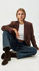 Bota corta de cuero vacuno color marrón oscuro, con taco cuadrado de madera y punta cuadrada. Presenta un diseño minimalista con cierre lateral interno y caña con elástico.