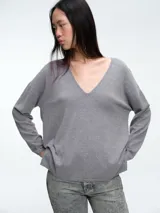 Sweater de punto gris con escote en V profundo, hombros caídos y mangas largas. Presenta un diseño de calce relajado con sutiles micro lentejuelas integradas en el tejido.