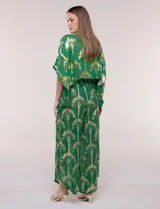 Blusa verde de gasa con transparencia y estampado metalizado dorado, de silueta holgada y mangas cortas. Presenta escote en V con pechera tejida en crochet y apliques de borlas colgantes.