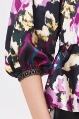 Camisa de satén con estampado floral abstracto en tonos violeta, fucsia, turquesa y negro. Presenta mangas abullonadas con puños elásticos y un ajuste en la cintura mediante cordón.