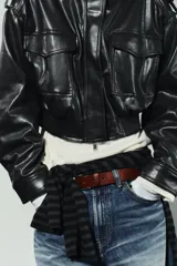 Cazadora corta de efecto piel color marrón oscuro, con cuello subido, manga larga con trabillas en los hombros, bolsillos con solapa en el delantero y cierre frontal con cremallera y botones a presión ocultos por solapa.