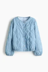 Campera acolchada ligera de denim en mezcla de algodón y lyocell, modelo Divided de H&M. Presenta cuello redondo, cierre frontal con botones a presión, hombros ligeramente caídos, mangas abullonadas y elástico revestido en los puños y el dobladillo inferior. Diseño pespunteado con ondas.
