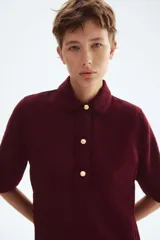 Vestido corto de tejido bouclé color bordó, con corte evasé, cuello camisero y tapeta de botones dorados. Posee mangas cortas y costuras princesa tanto adelante como atrás.