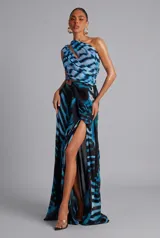 Vestido largo de fiesta con estampado etéreo en tonos azules y negros, escote asimétrico de un solo hombro con detalle cruzado y abertura en el abdomen con hebilla dorada. Presenta falda larga con tajo lateral pronunciado.