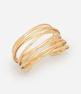 Pulsera rígida tipo brazalete de metal dorado, con diseño abierto y estructura de múltiples varillas paralelas que se entrelazan de forma asimétrica.