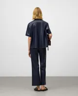 Pantalón negro de efecto cuero, corte flare o acampanado, largo hasta el tobillo. Presenta bolsillos de vivo en la espalda y cierre lateral de cremallera.