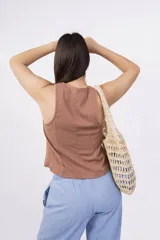 Chaleco corto sin mangas color verde salvia, confeccionado en tela perforada (broderie o calado). Presenta escote en V con lazos ajustables en el centro frontal.